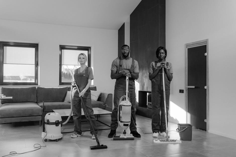 Two professional cleaning specialists from Dollis Hill Carpet Cleaners are in a bright, modern room with large windows allowing natural light to illuminate the space. They are wearing white uniforms a
